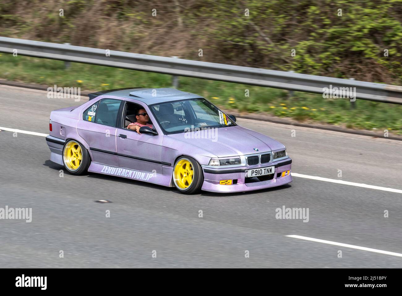 Années 1997 90, années 90, mauve BMW 316 i se 316i essence berline 1596cc (ZeroTraction.JP) voiture sur mesure avec des roues jaunes ; voyageant à grande vitesse sur l'autoroute M6 dans le Grand Manchester, Royaume-Uni Banque D'Images