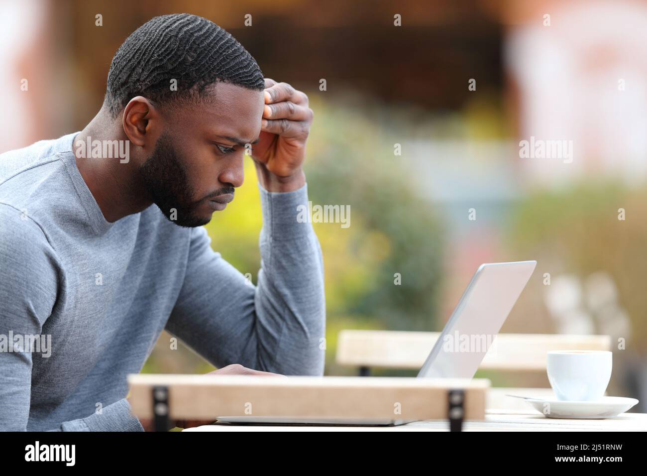 Profil d'un homme inquiet avec une peau noire vérifiant ordinateur portable dans une terrasse de bar Banque D'Images