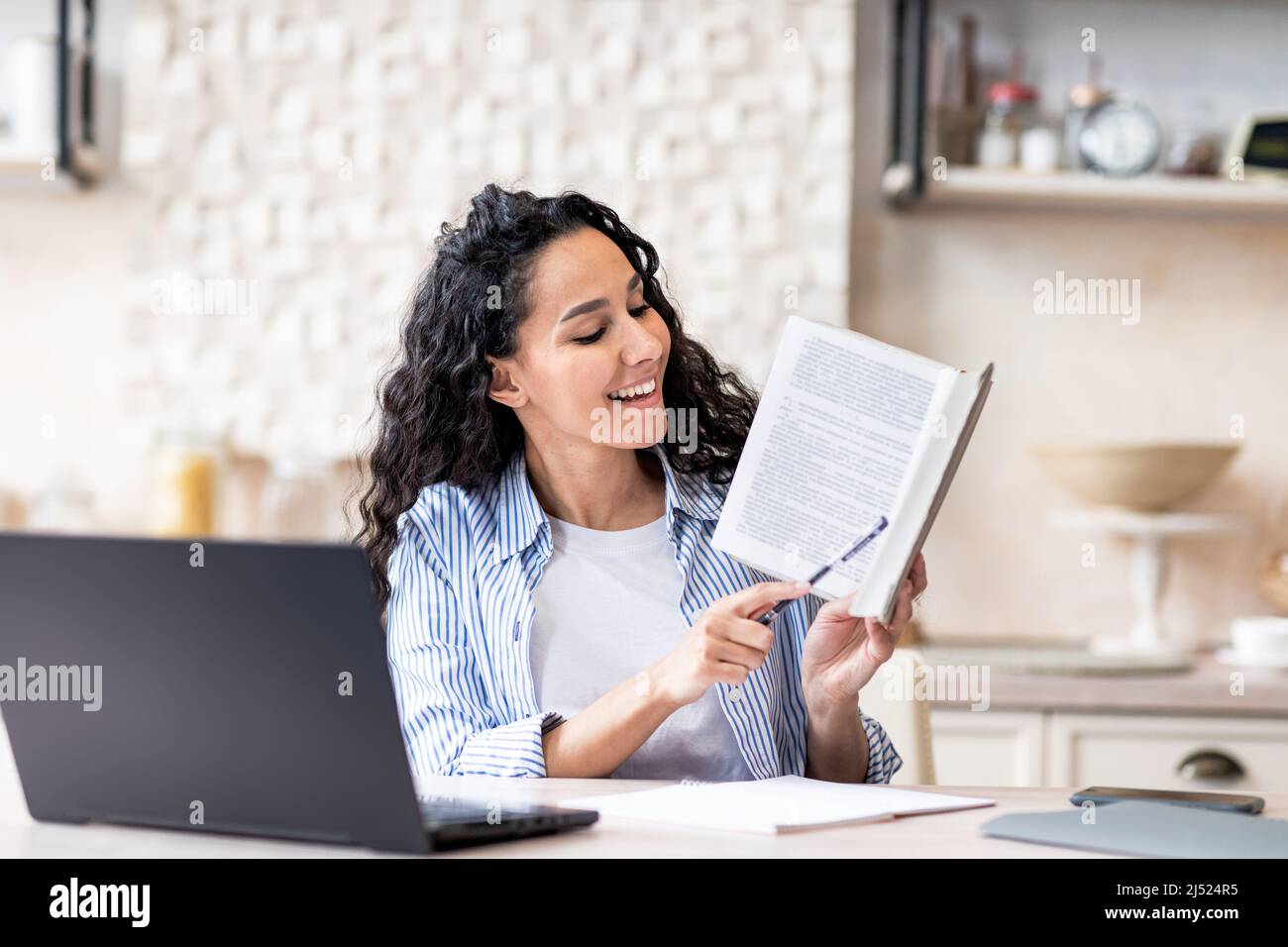 Une femme heureuse ayant une réunion virtuelle via un ordinateur portable, donnant des leçons en ligne de la maison, assis dans la cuisine intérieure Banque D'Images