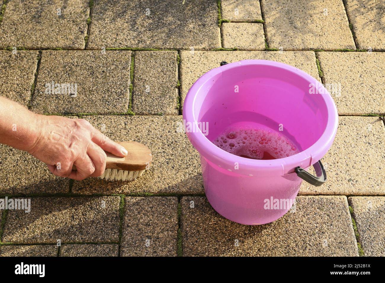 Nettoyage traditionnel des pavés sales dans le jardin avec de l'eau et une brosse. Travailleur à domicile Banque D'Images