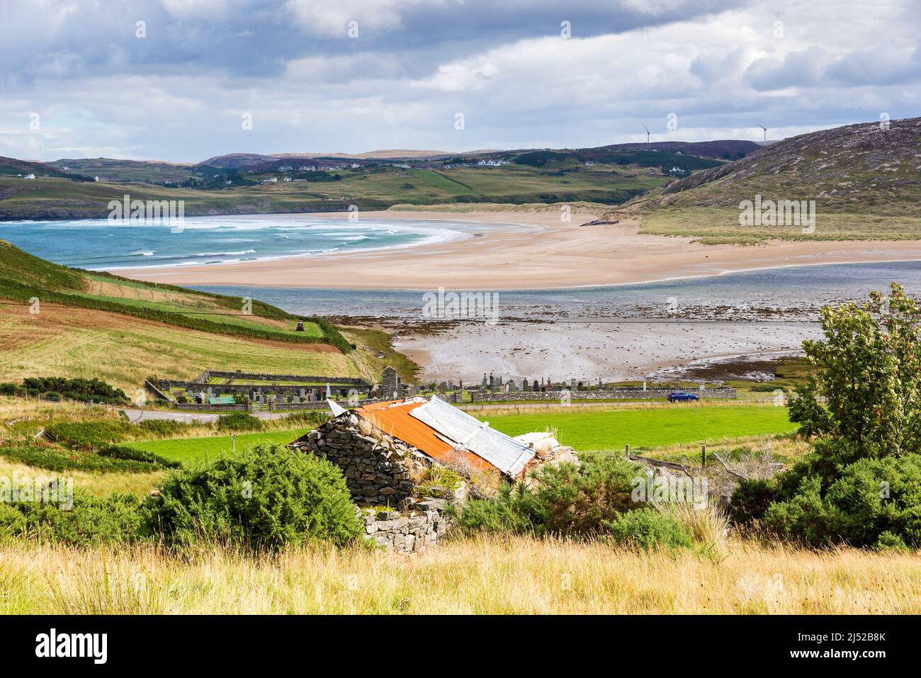 Un vieux bâtiment en pierre avec un toit en étain surplombe la grande plage de sable déserte et la mer turquoise brillante de la baie de Torrisdale, par une journée ensoleillée. Banque D'Images