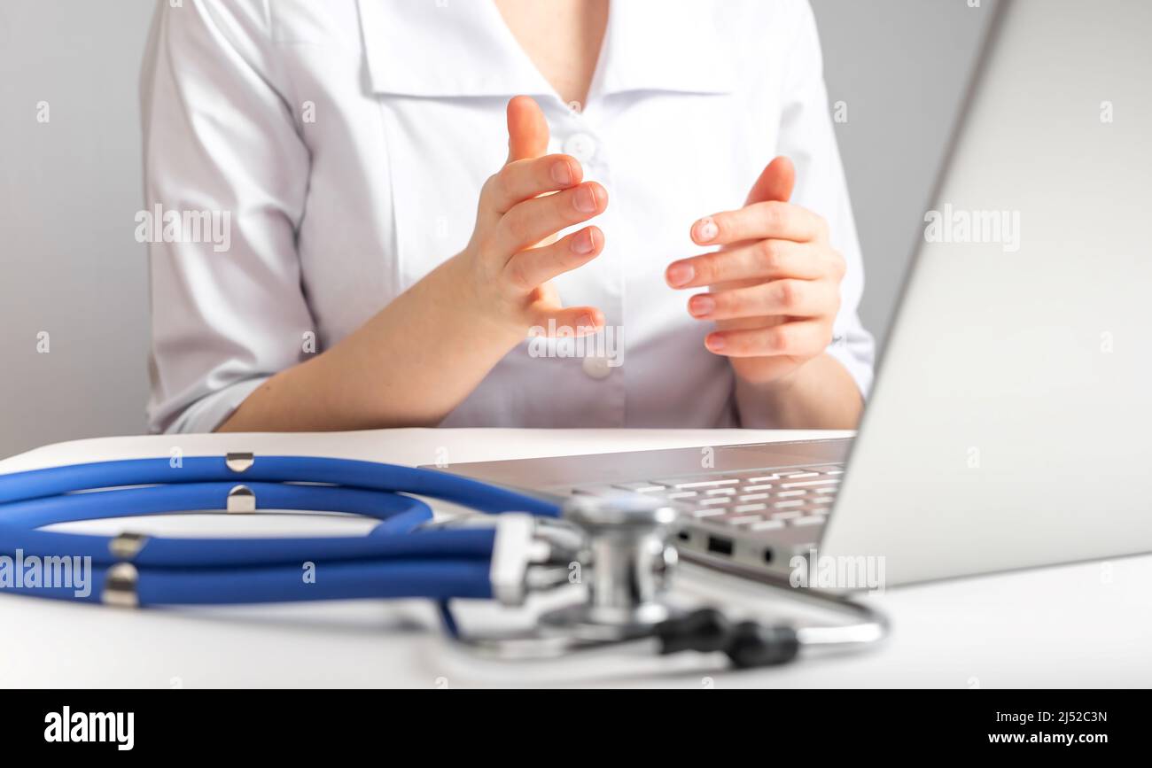 Médecin donnant consultation en ligne au patient. Concept de santé et de télémédecine. Examen à distance des clients et traitement des maladies. Femme en blouse de laboratoire assise au bureau avec ordinateur portable et stéthoscope. Photo Banque D'Images