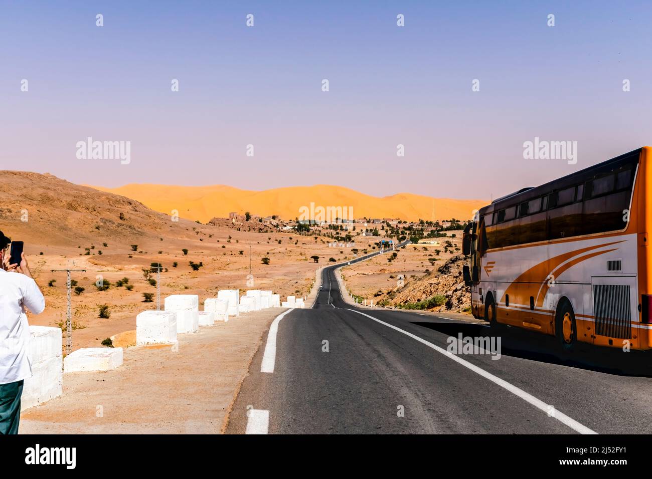 Un bus garé et un touriste méconnaissable prenant une photo avec un smartphone de la dune de sable et de la montagne reg, des clous en béton blanc le long de la route. Banque D'Images