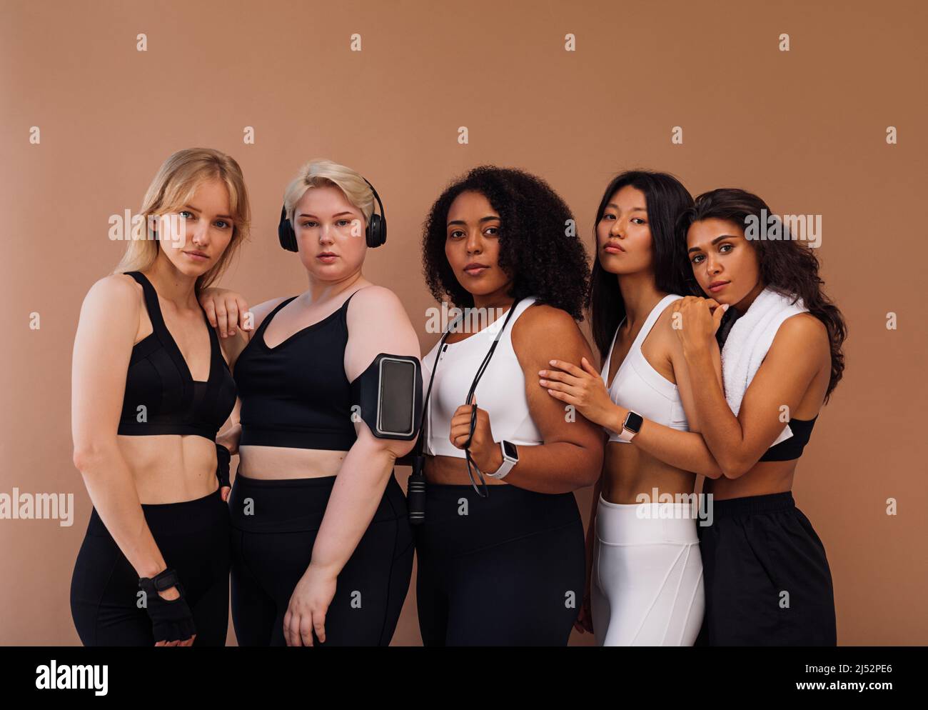 Groupe de cinq femmes en vêtements de sport avec des accessoires de fitness debout ensemble. Diverses femmes se posant ensemble en studio. Banque D'Images