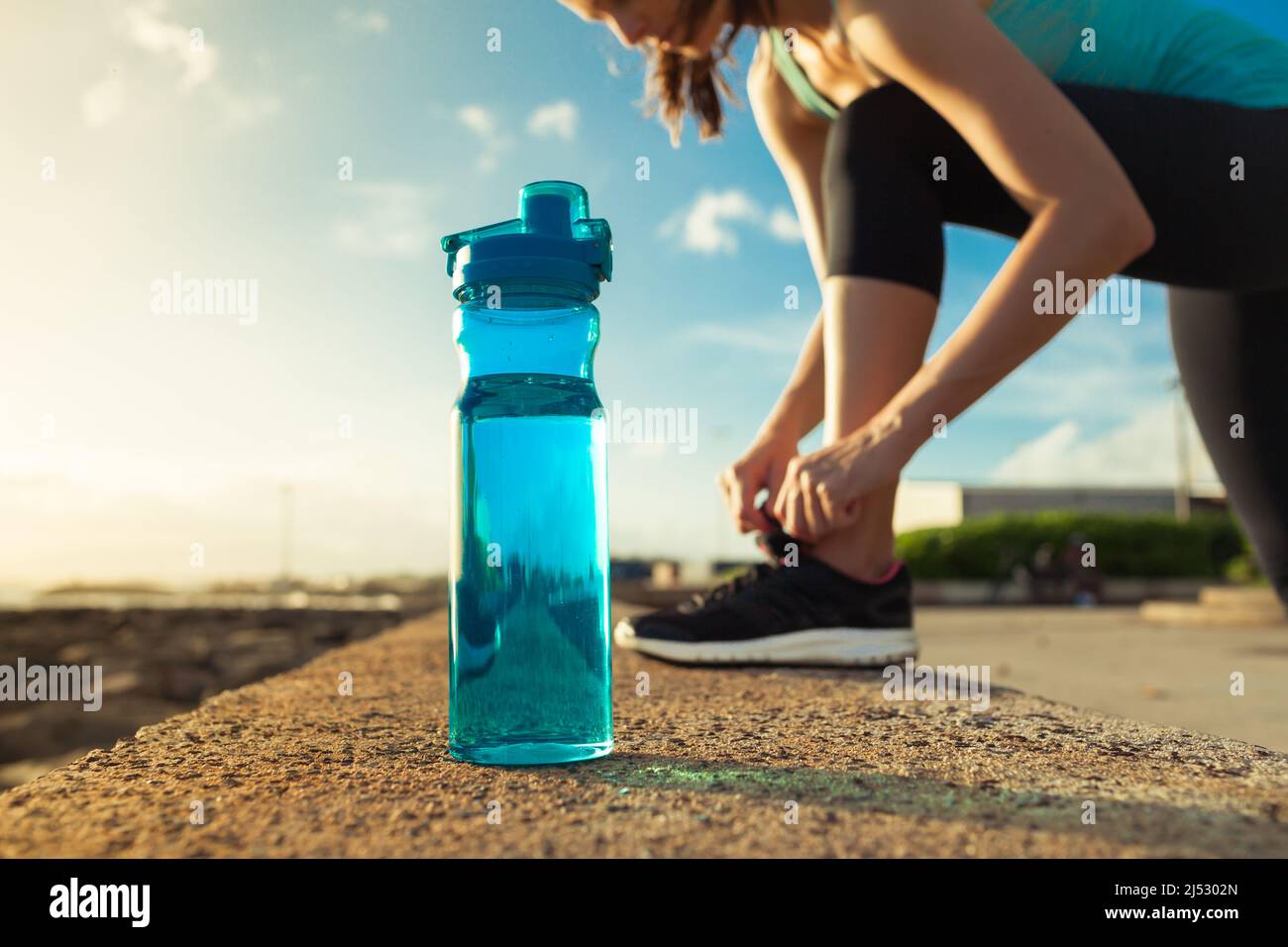 Concept de l'eau potable. Une femme qui attache sa chaussure à côté d'une bouteille d'eau. Banque D'Images