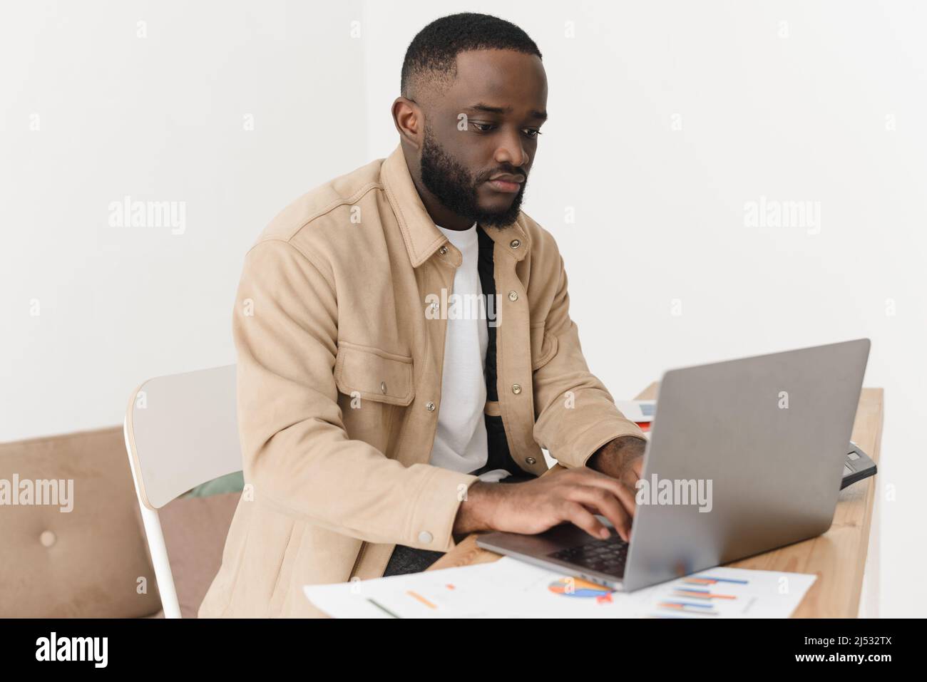 Jeune afro-américain concentré comptant les dépenses et gardant les dossiers sur ordinateur portable, les comptes de banque de papier sont sur la table. Le modèle masculin gère tous les mois Banque D'Images