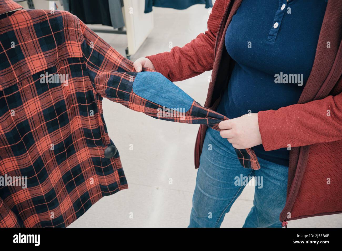 La femme enceinte choisit la chemise à carreaux en flanelle en magasin pour acheter. Les mains en gros plan Banque D'Images