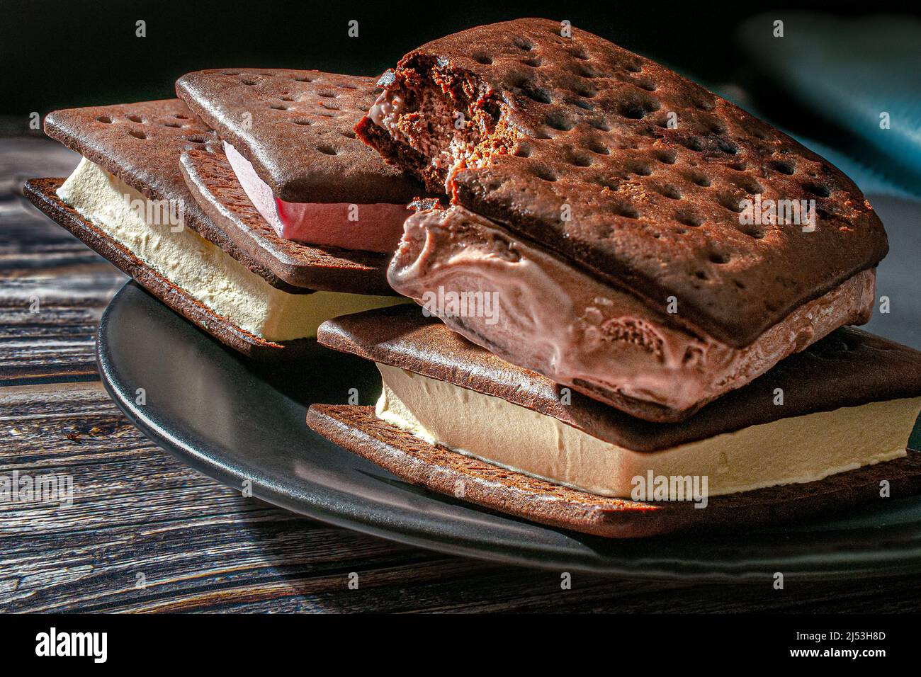 Sandwiches à la crème glacée sur une assiette noire avec une serviette bleue au fond sur une table en bois avec un fond noir, éclairée par une lumière de fenêtre Banque D'Images