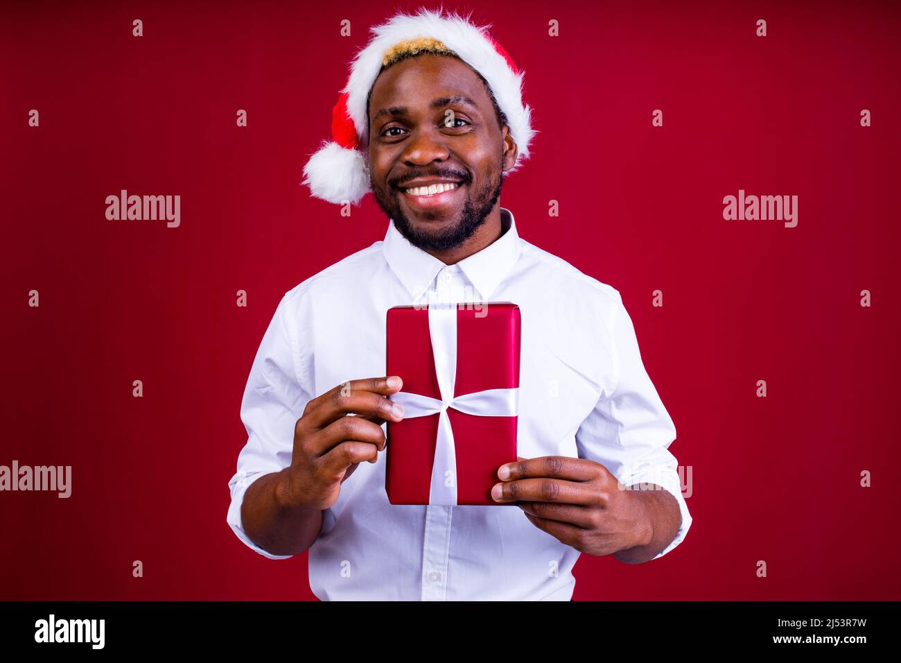 homme latino-hispanique portant un chapeau santas sur fond rouge studio Banque D'Images