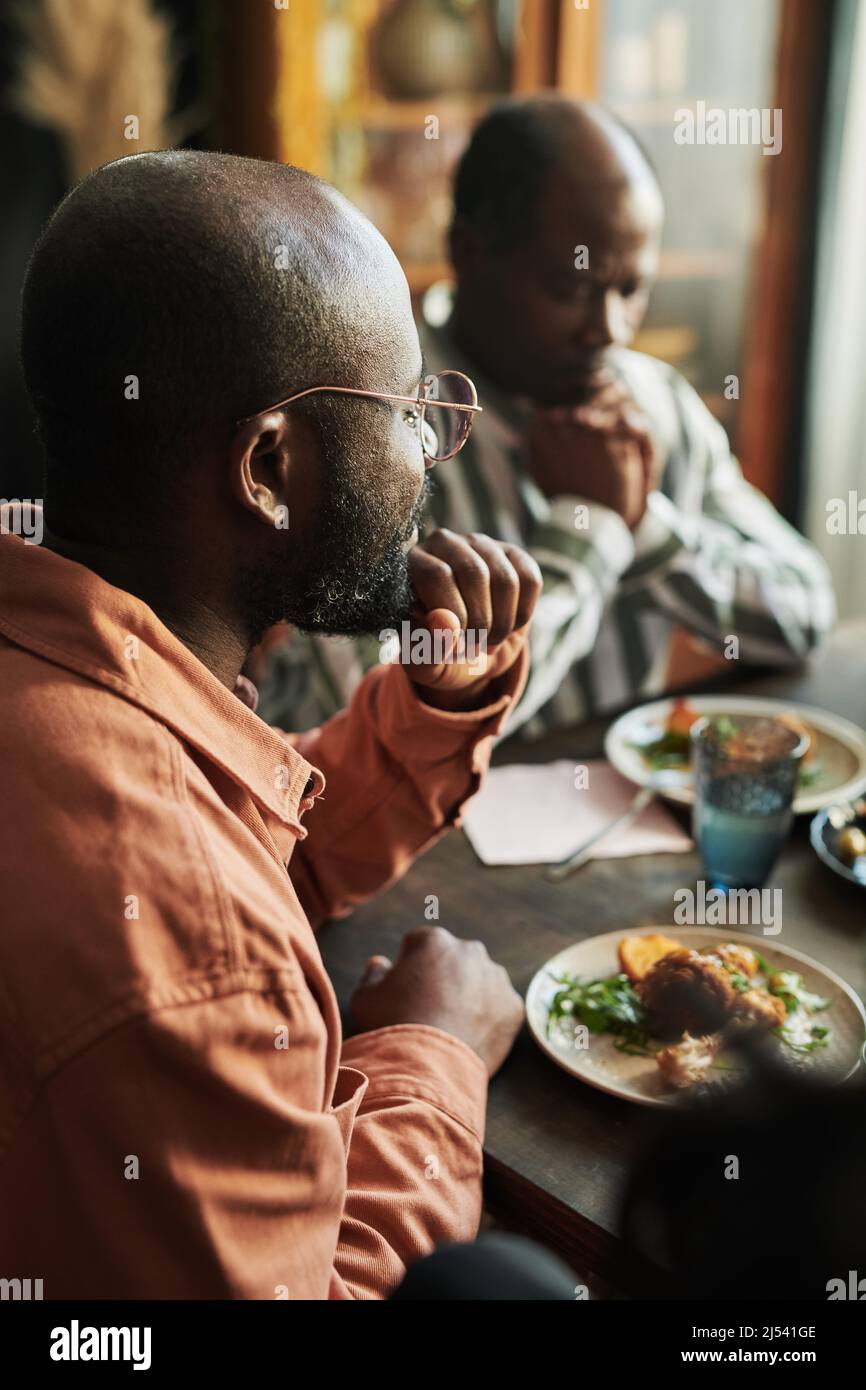 Homme africain en lunettes assis à table et dîner avec sa famille à la maison Banque D'Images