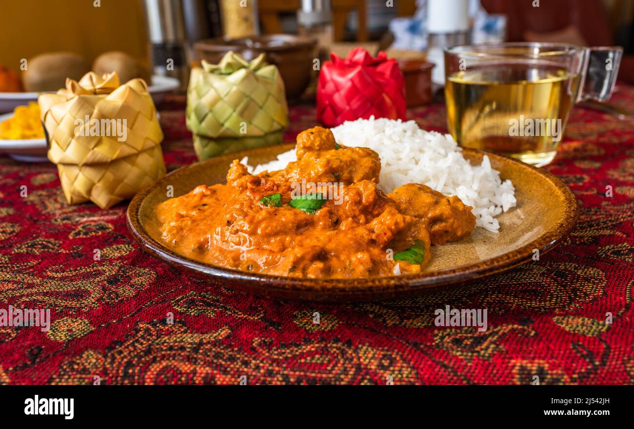 Poulet tikka masala avec riz sur plaque, 3 boîtes d'épices en bambou, tasse de thé sur nappe rouge sur table. Déjeuner ou dîner indien. Banque D'Images