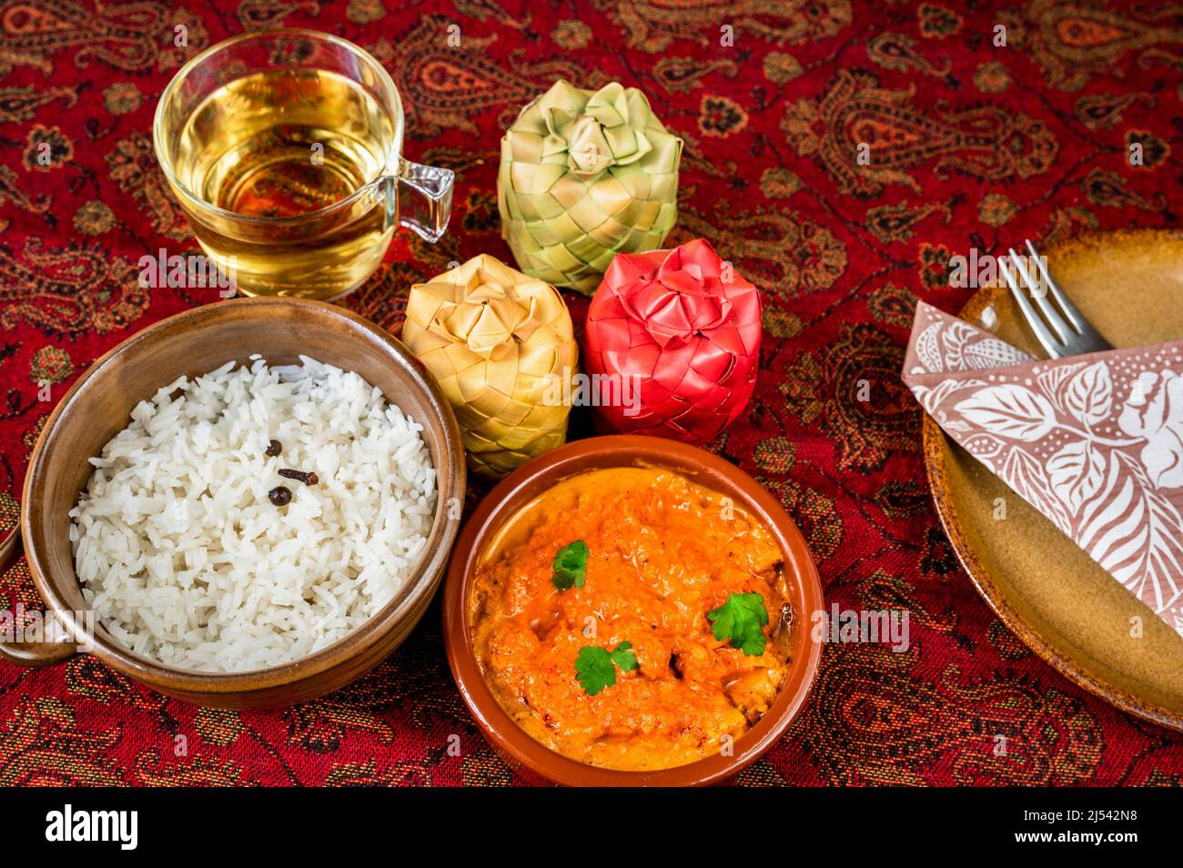 Poulet tikka masala, riz cuit dans un bol de 2, tasse de thé, contenant de 3 épices en bambou, partie de l'assiette, serviette et fourchette sur nappe rouge. Cuisine indienne. Banque D'Images