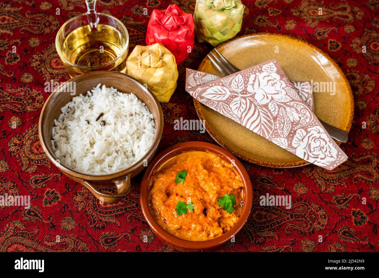 Poulet tikka masala avec riz cuit dans un bol de 2, tasse de thé, contenant de 3 épices en bambou, assiette avec serviette et fourchette sur nappe rouge, gros plan. Cui indien Banque D'Images