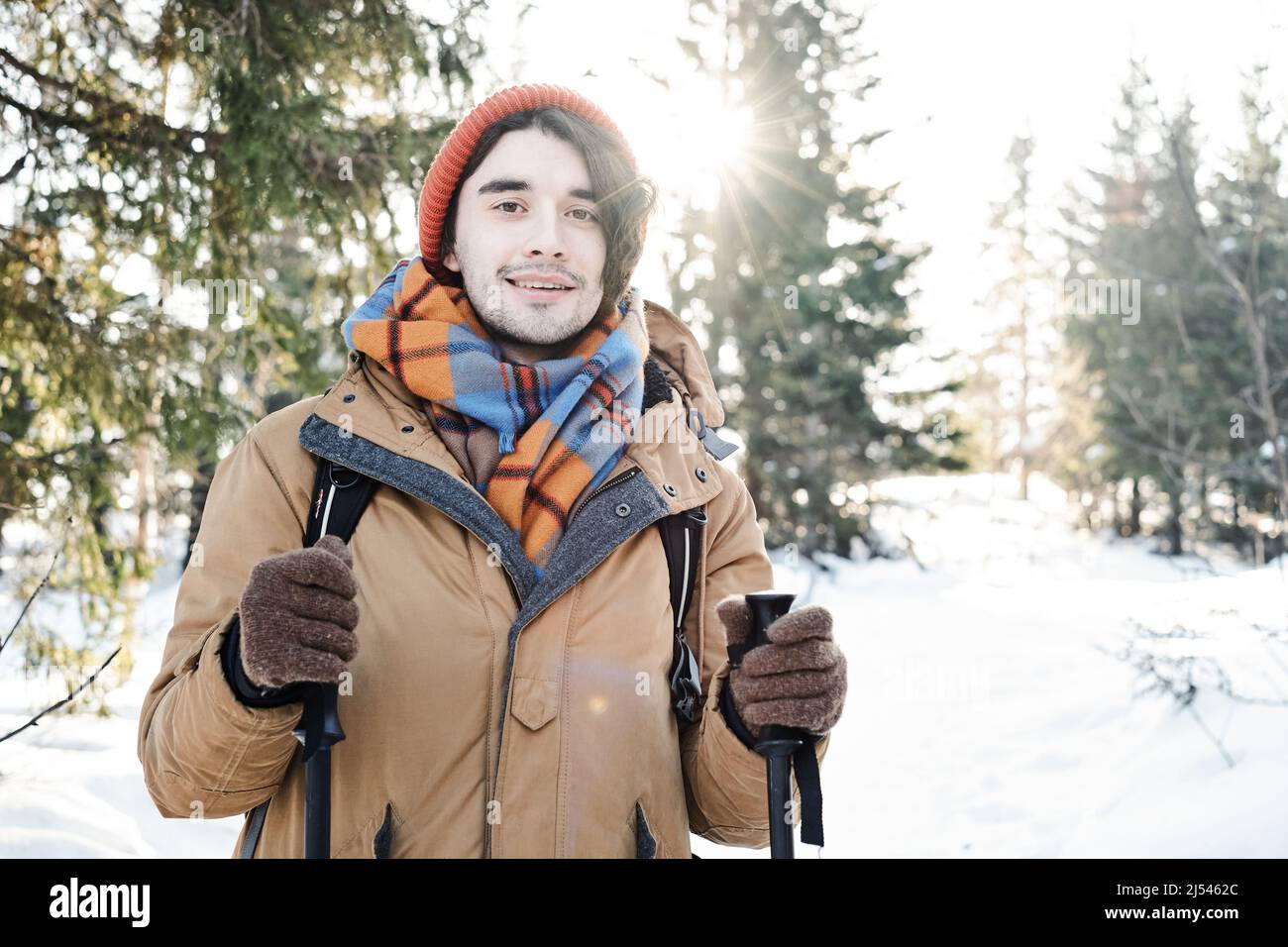 Portrait d'un jeune homme joyeux portant des vêtements élégants avec sac à dos debout quelque part en montagne le jour d'hiver ensoleillé Banque D'Images