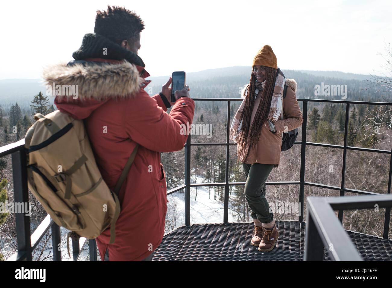 Jeune touriste noir debout sur la terrasse d'observation au sommet de la montagne en prenant des photos de sa belle petite amie Banque D'Images