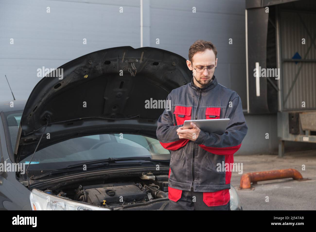 Mécanicien caucasien en uniforme utilisant un PC tablette au poste de réparation de voiture. Entretien de la voiture Banque D'Images