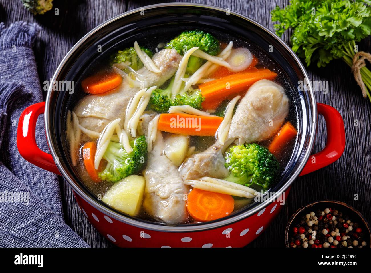 soupe de printemps au poulet avec brocoli, carottes, panais, poireaux et pâtes dans un pot rouge sur une table en bois sombre, gros plan Banque D'Images