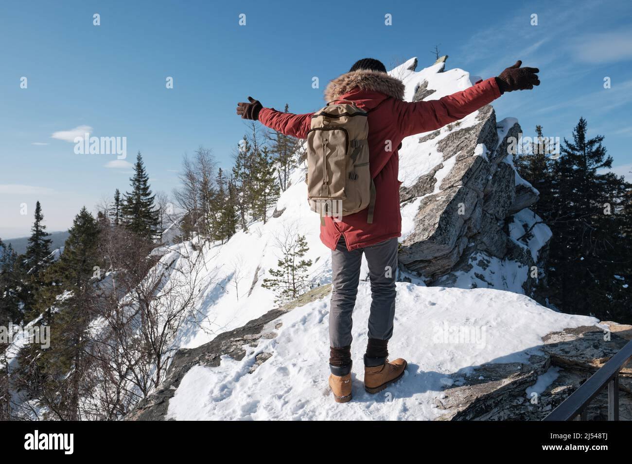 Jeune homme méconnaissable portant des vêtements chauds et un sac à dos voyageant en montagne avec les bras ouverts Banque D'Images