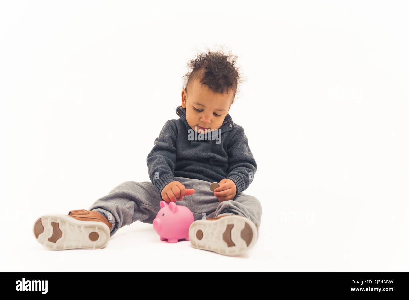 Un jeune enfant met des pièces de monnaie dans une banque de porc, sur fond blanc isolé. Photo de haute qualité Banque D'Images