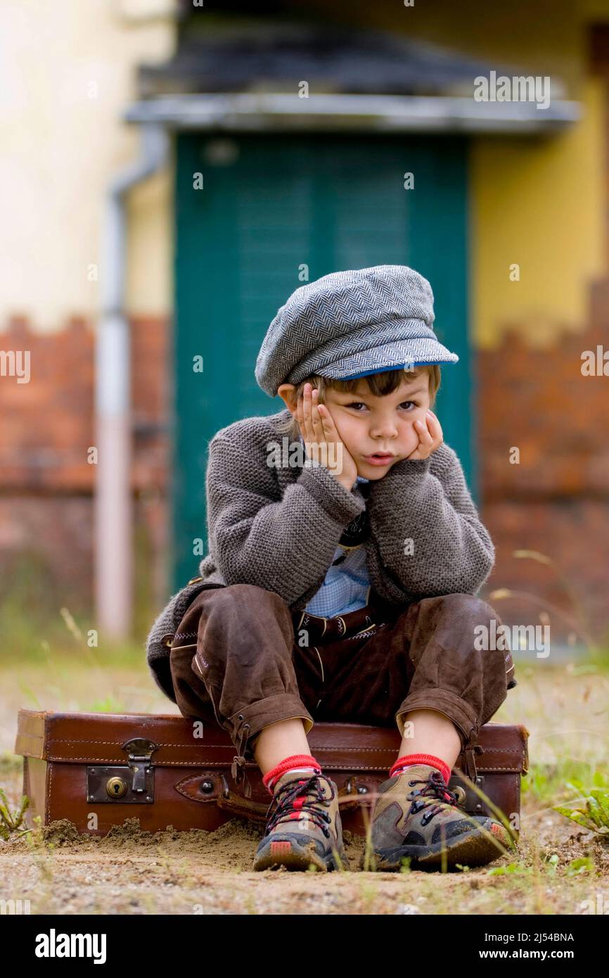 Petit garçon malheureusement assis sur une valise en cuir, Allemagne Banque D'Images
