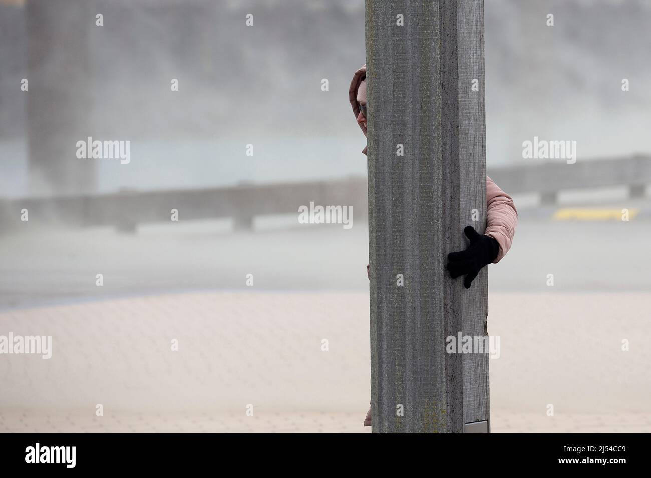 Femme à un poste en bois dans la tempête sur la plage de sable, Hurricane Eunice, Zeynep, 02/18/2022, Belgique, Flandre Occidentale, Nieuwpoort Banque D'Images
