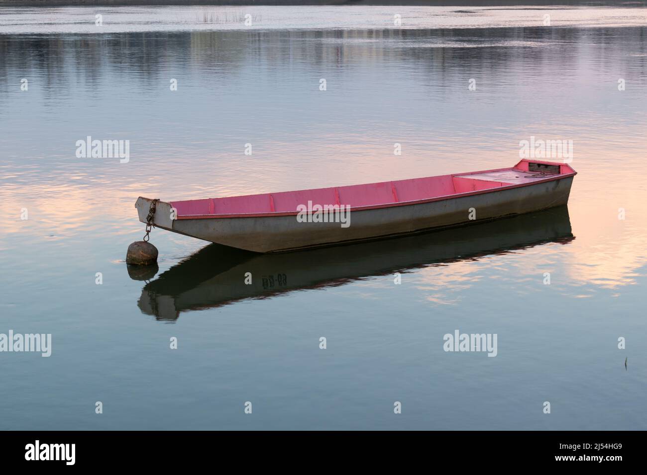 Bateau en métal ancré de couleur pourpre et grise, ciel et nuages se reflétant dans l'eau ondulée Banque D'Images