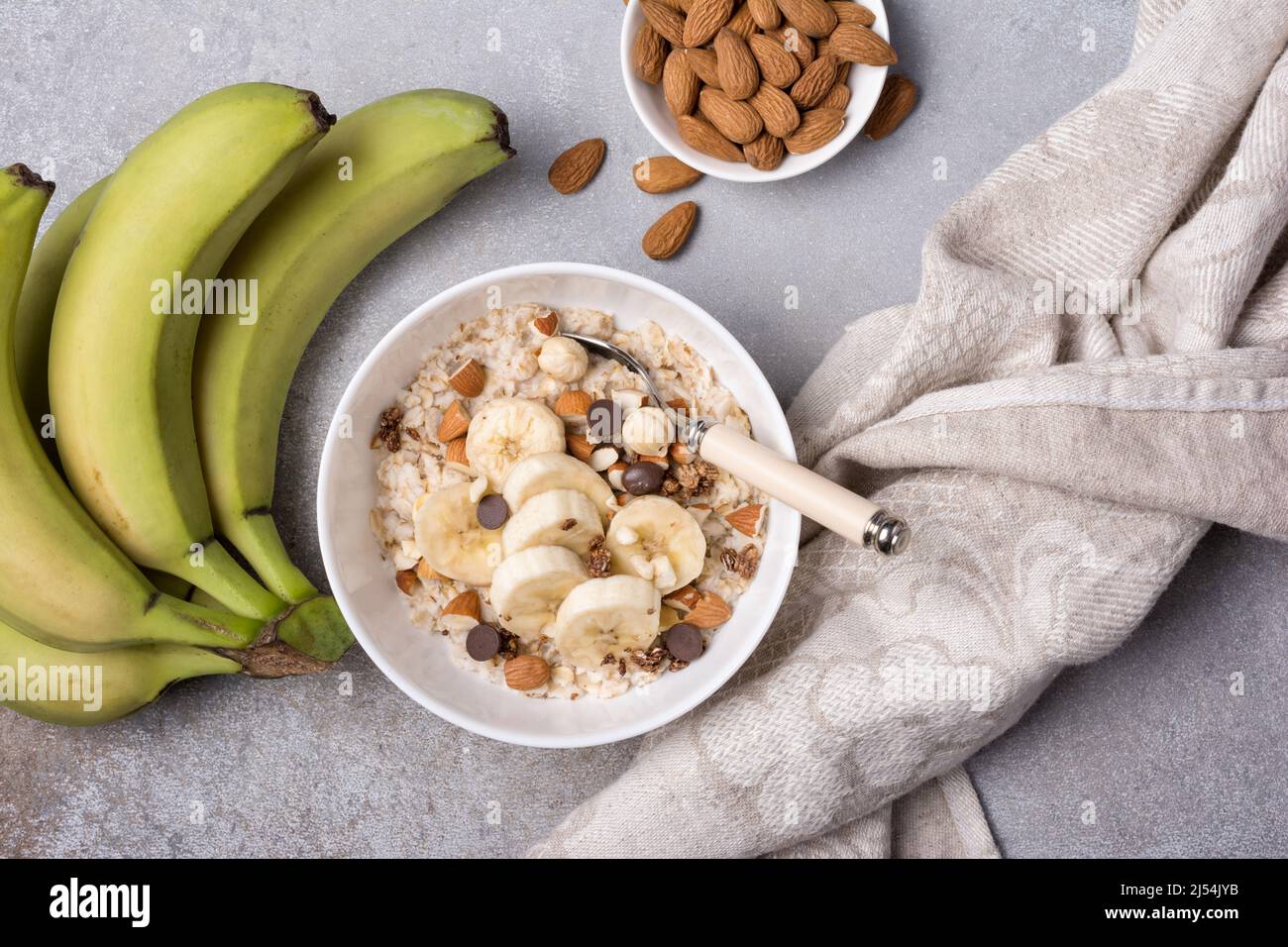 Vue de dessus des flocons d'avoine avec des tranches de bananes fraîches, des amandes, des noisettes et des gouttes de chocolat pour un petit déjeuner sain sur fond de béton gris Banque D'Images