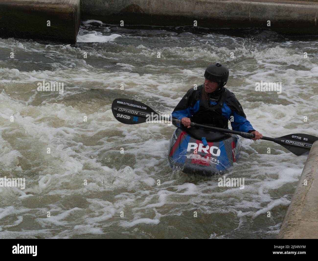 Jeune garçon en kayak s'attaquant à l'eau blanche de Holme Pierrepont Country Park Nottingham Angleterre Grande-Bretagne pagayer contre l'actuel Centre national des sports nautiques Banque D'Images