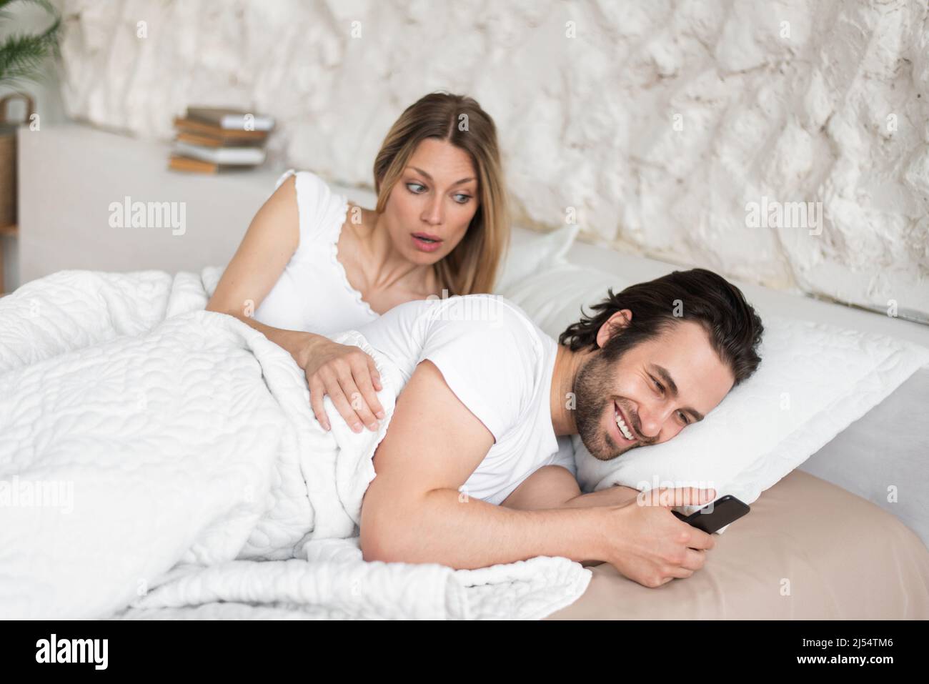 Une jeune femme choquée voit son mari envoyer des messages à son amant sur son smartphone tout en étant couché au lit à la maison Banque D'Images