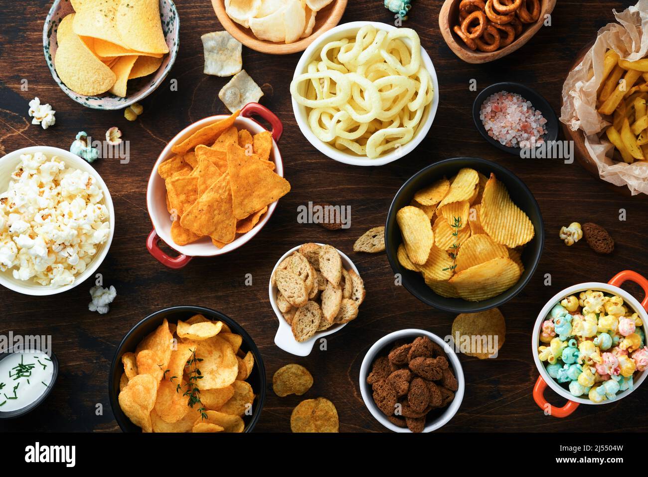 Aliments ou collations malsains. Tous les en-cas classiques de pommes de terre avec des arachides, du pop-corn et des rondelles d'oignon et des bretzels salés dans des assiettes à bol sur fond de bois ancien. Banque D'Images