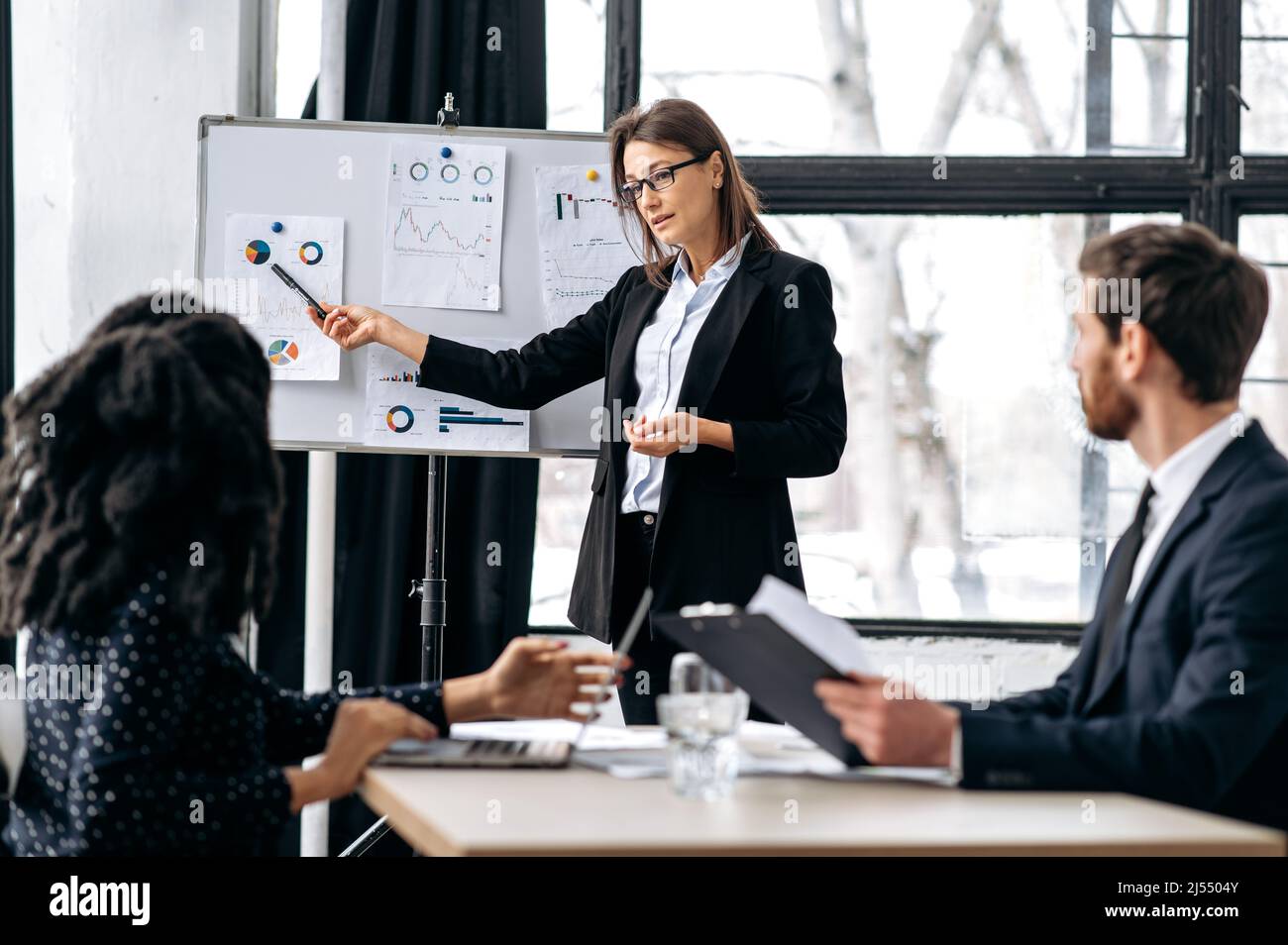 Réunion d'affaires, remue-méninges de collègues d'affaires de différentes nationalités dans un bureau moderne, femme boss intelligent indique la stratégie financière aux partenaires, analyse rapport et bénéfice, montre praphs Banque D'Images