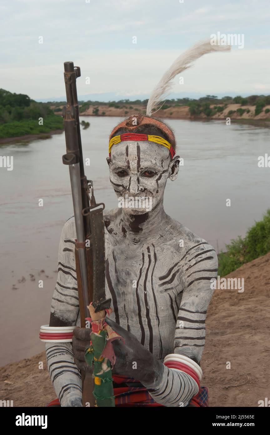 Karo guerrier aux peintures du corps et du visage et au fusil assis sur son appui-tête, la vallée de la rivière Omo, dans le sud de l'Éthiopie Banque D'Images