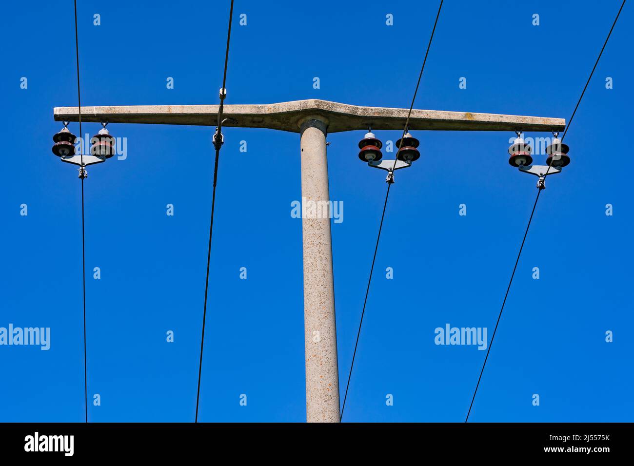 Lignes électriques et isolateurs sur un poteau en béton moyenne tension contre un ciel bleu Banque D'Images