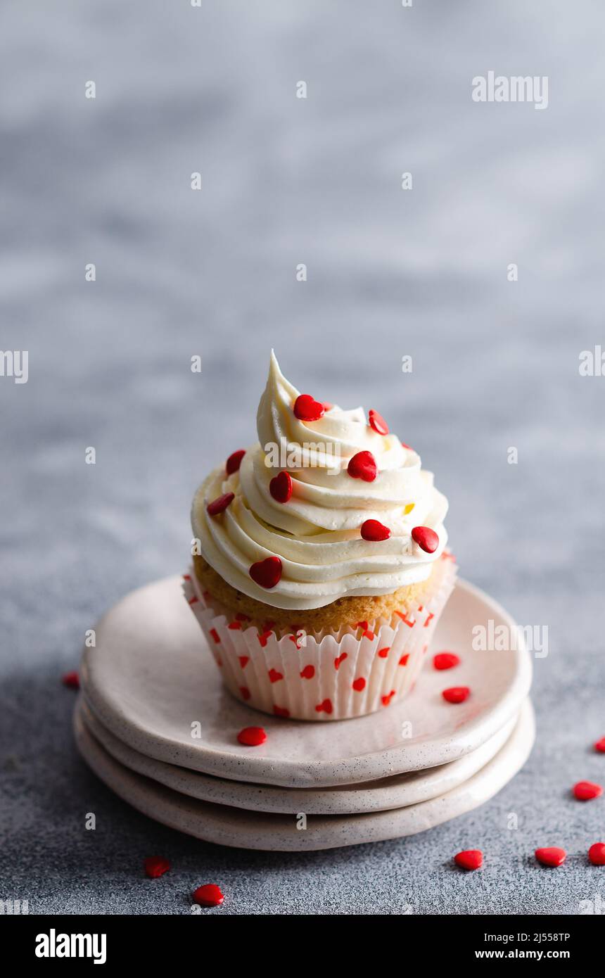 Muffin vanille avec glaçage au beurre et coeurs de sucre rouge sur trois assiettes et fond gris avec espace copie. Banque D'Images