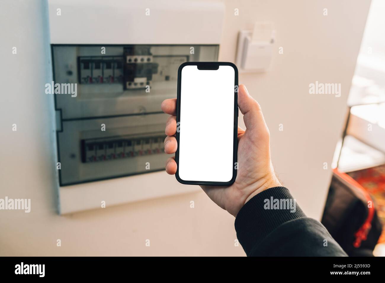 Électricien tenant un smartphone avec écran tactile maquette vierge devant le boîtier de disjoncteur à la maison, mise au point sélective Banque D'Images