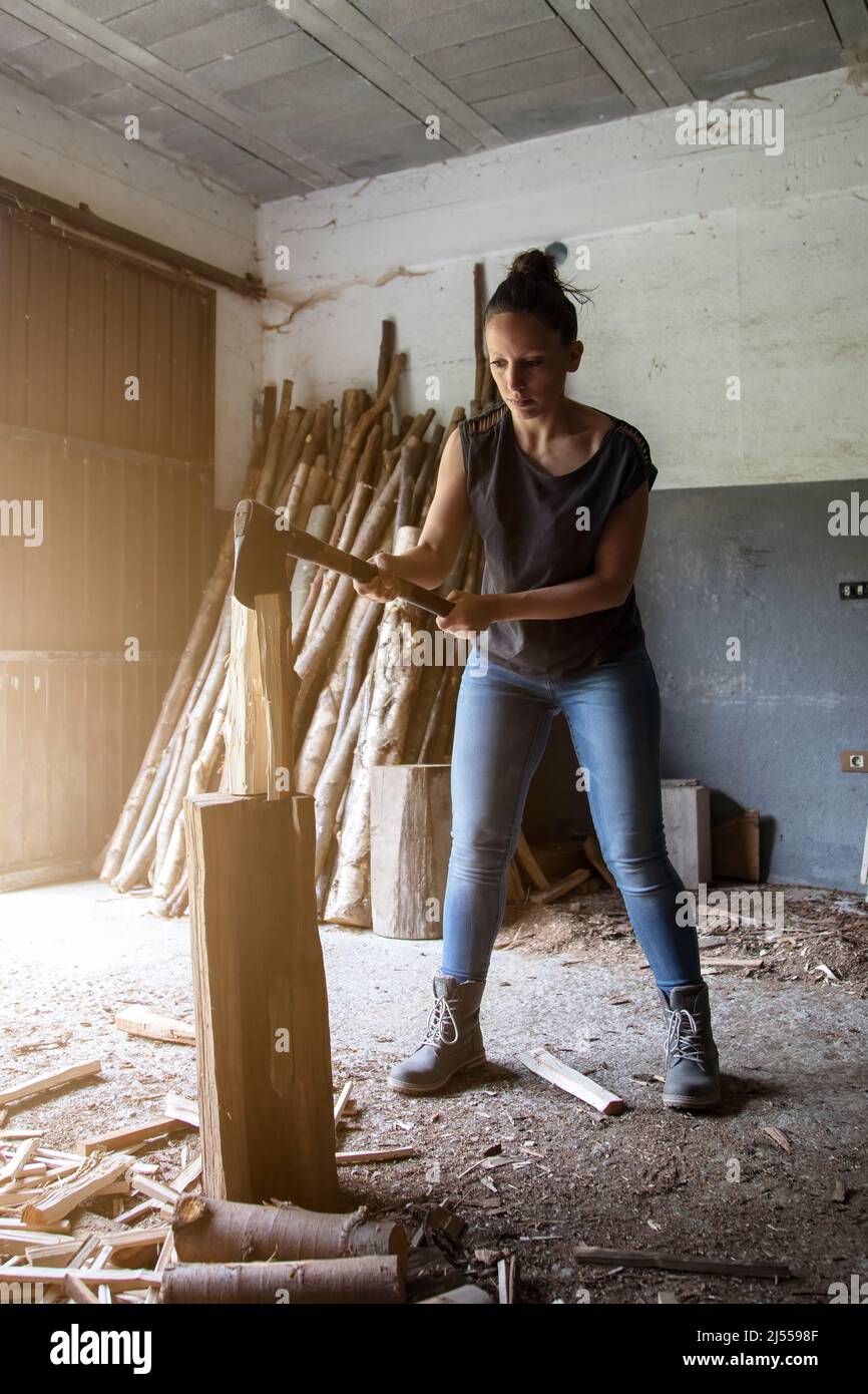 photo verticale d'une fille se concentrant sur la séparation du bois de chauffage avec une hache dans ses mains pour stocker et faire le feu en hiver. vie rurale. Espace pour la copie Banque D'Images