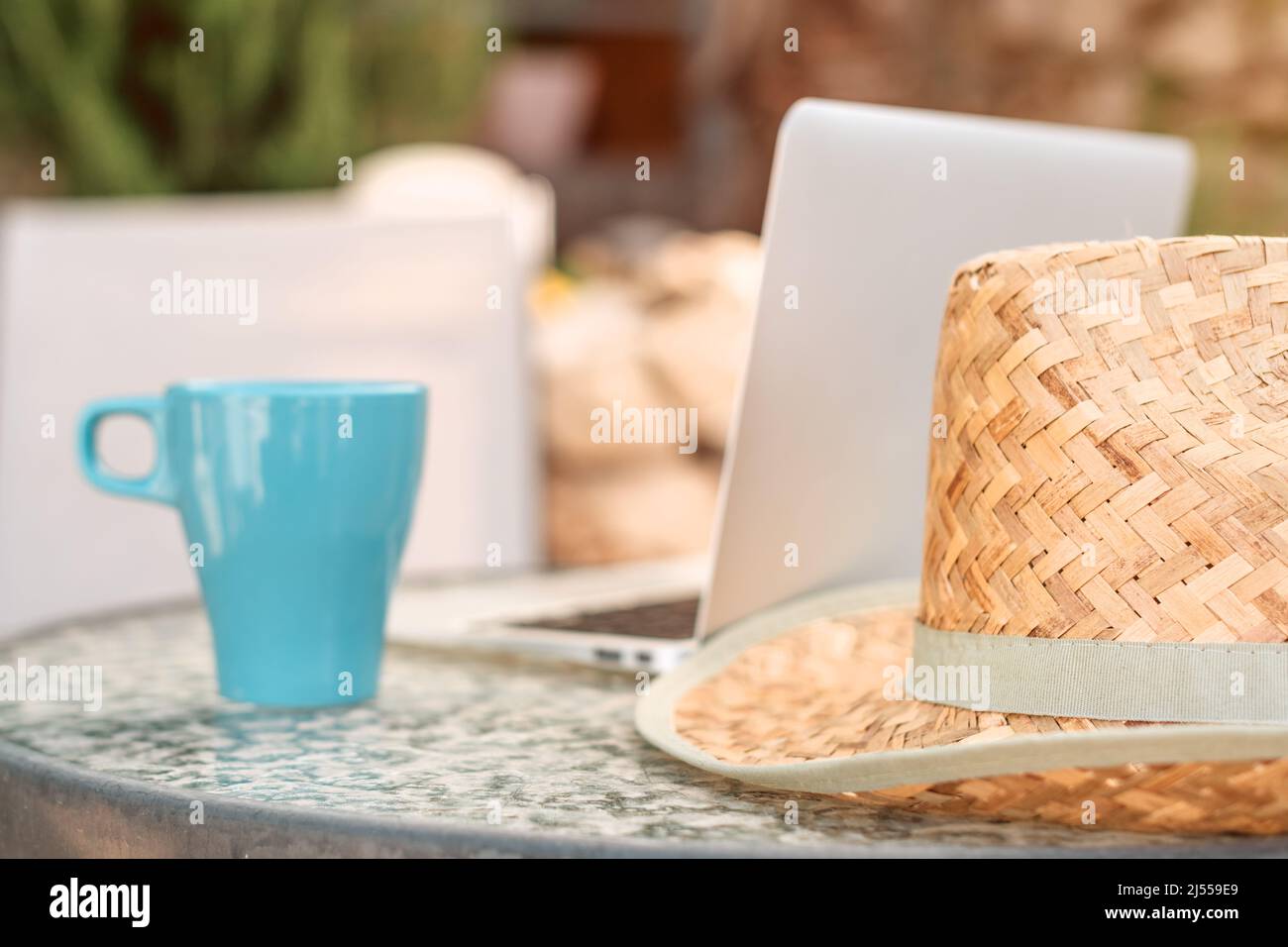 Travail sur la terrasse de l'arrière-cour de vacances espace de travail avec ordinateur portable, tasse de café et chapeau de paille de plage Banque D'Images
