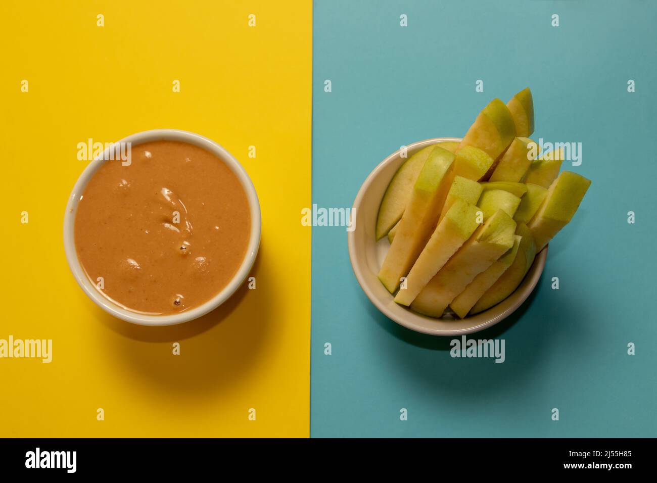 Tranches de pomme verte et beurre d'arachide dans une tasse. Arrière-plan jaune et bleu. Banque D'Images