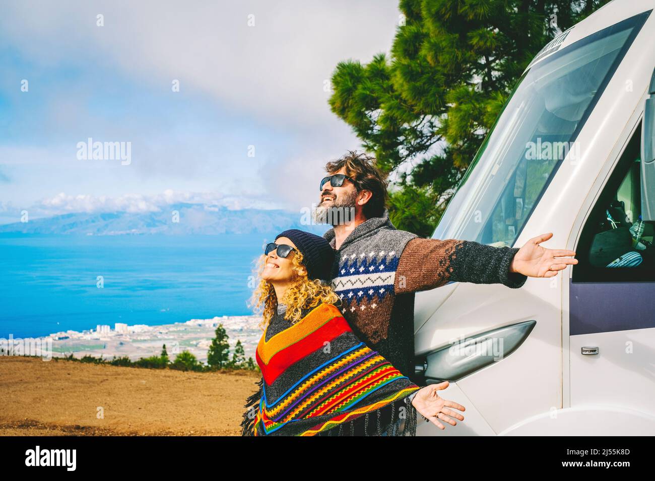 Concept de la durée de vie des fourgonnettes et de la destination des voyages. L'homme et la femme se réjouissent d'une nouvelle arrivée dans la nature en ouvrant les bras contre leur nouveau camping-car moderne. Banque D'Images
