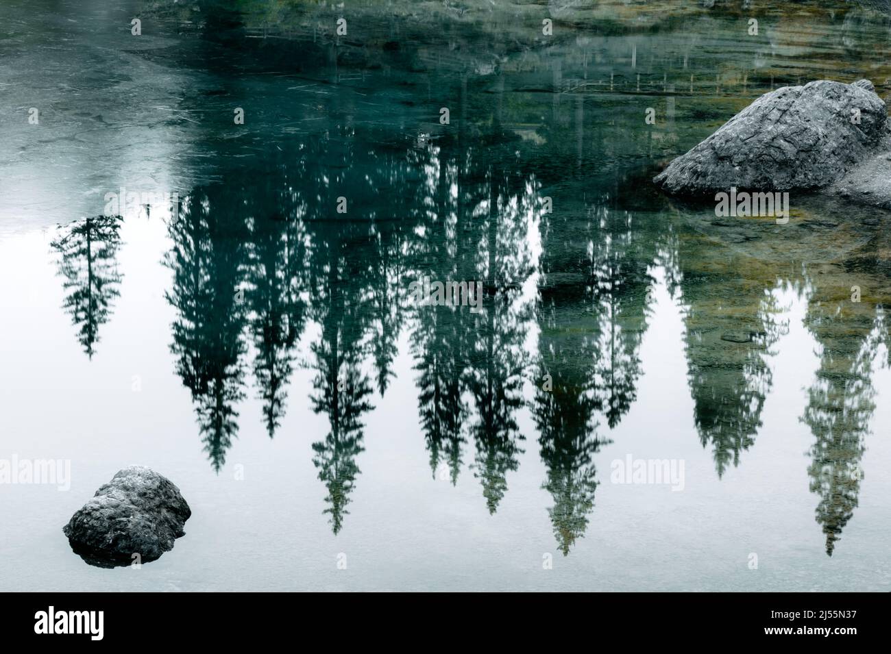 Eaux turquoises gelées du lac Carezza (Karersee) dans les Dolomites de l'Ouest, en Italie. Belle vue rapprochée avec reflets de pierres et de pins. Montagnes de dolomie, Tyrol du Sud, Italie. Photographie de paysage Banque D'Images
