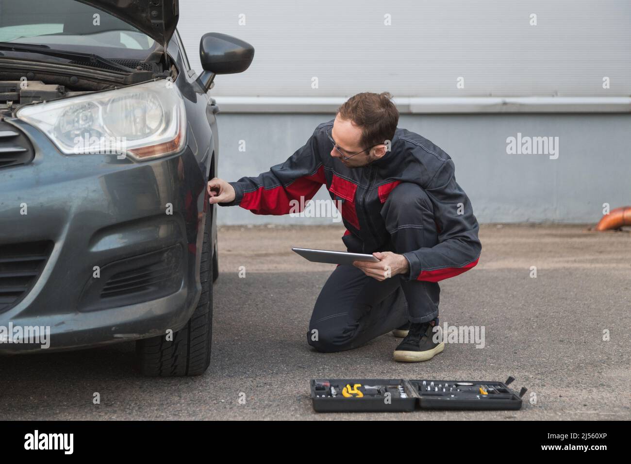 Mécanicien avec tablette PC électronique contrôlant les roues et les pneus pendant le travail dans le centre de réparation de voiture Banque D'Images