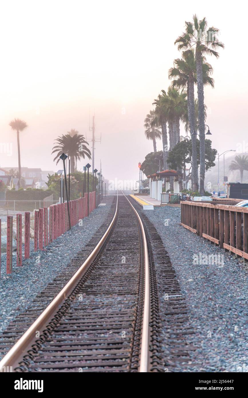 Voies de train avec barrière de poteaux et une vue de l'attente hangar le long des palmiers à San Clemente, CA Banque D'Images