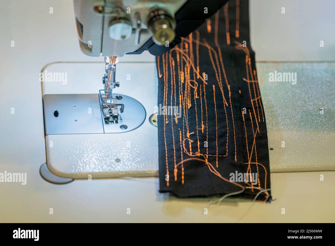 Gros plan de l'aiguille de la machine à coudre et du tissu cousus de fils orange Banque D'Images