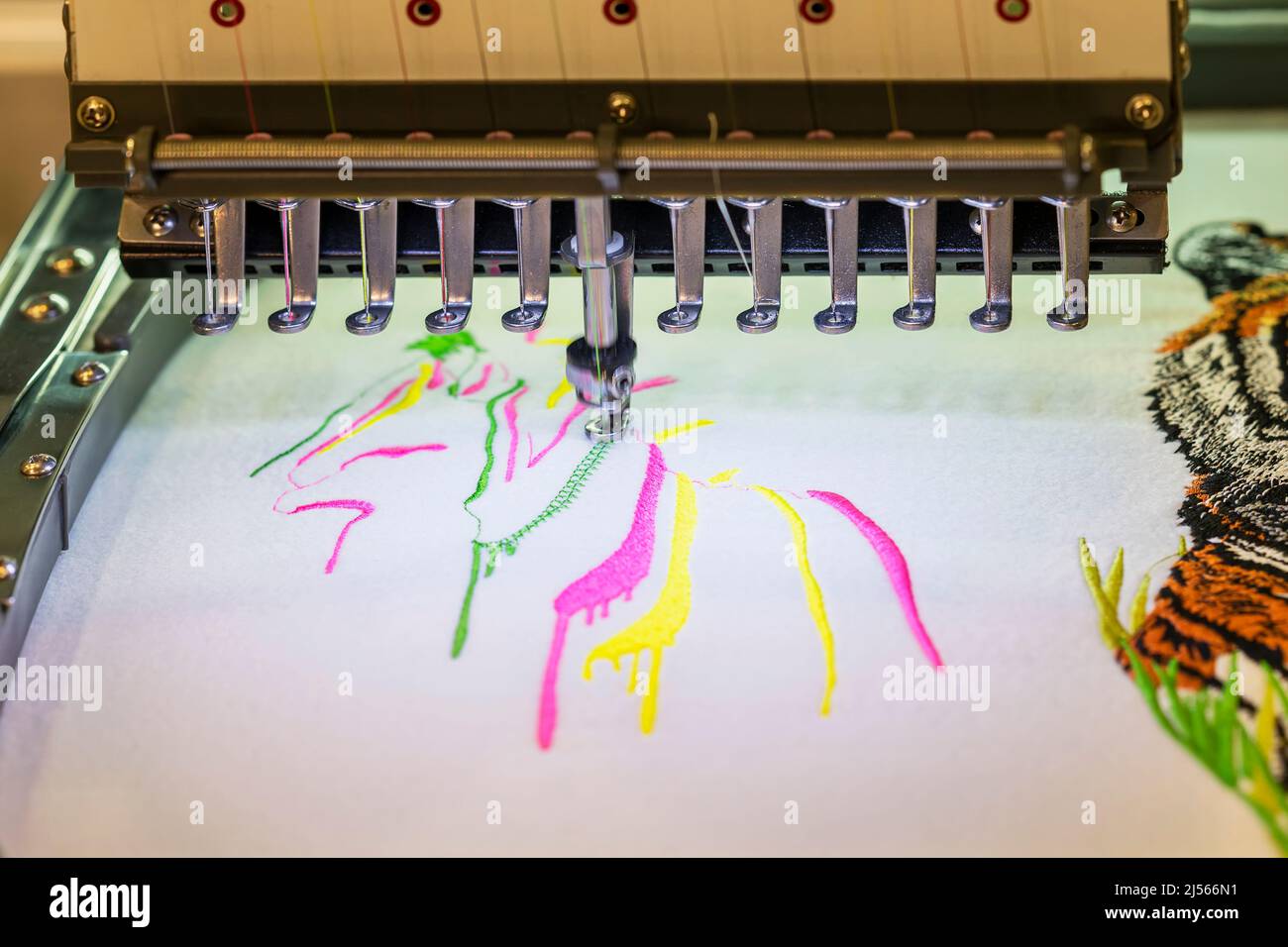Aiguilles d'une machine à broder industrielle et tissu avec coutures de fils multicolores gros plan Banque D'Images