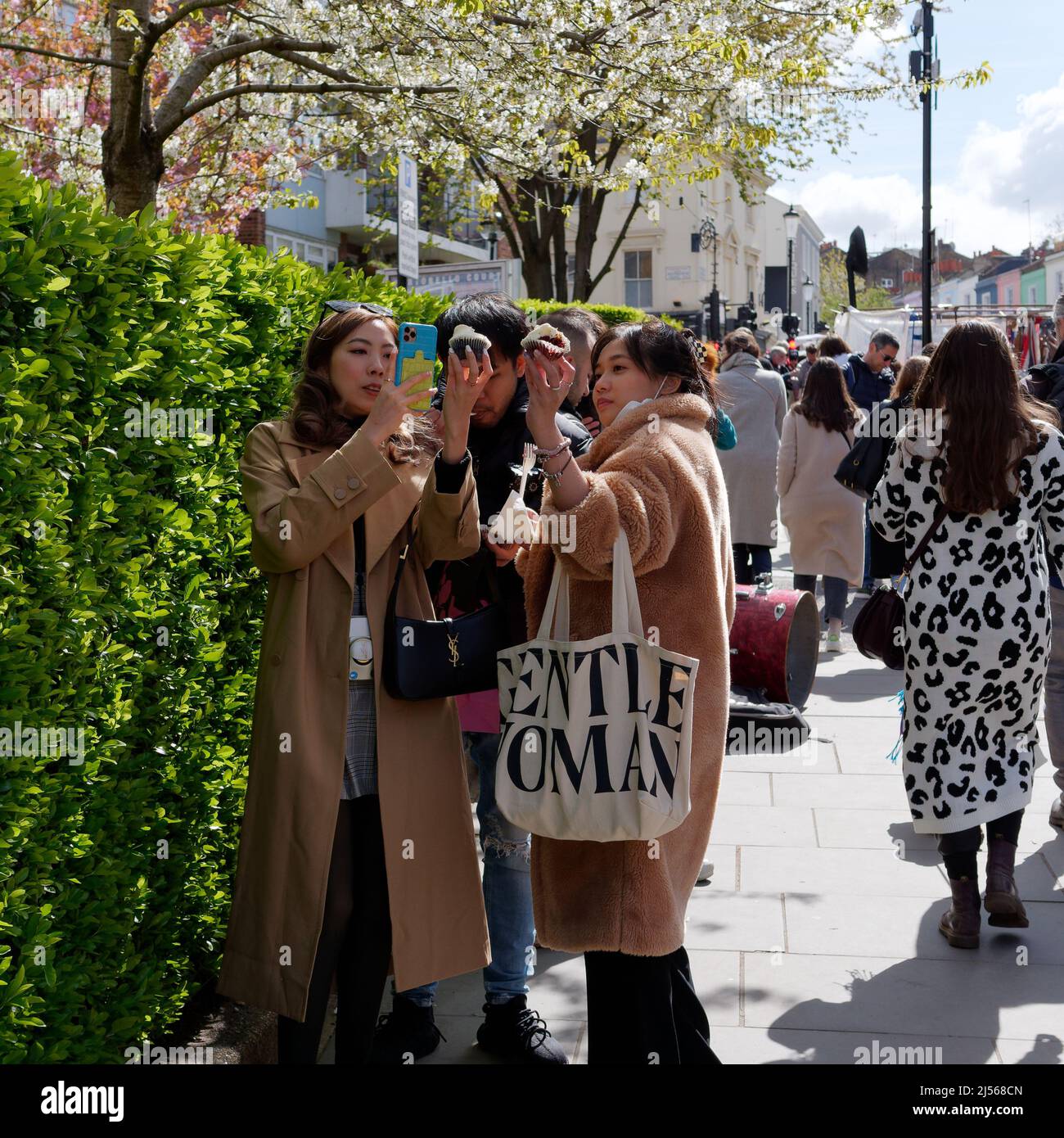 Londres, Grand Londres, Angleterre, avril 09 2022 : des femmes asiatiques prennent des photos de leurs gâteaux de tasse sur Portabello Road avec leur téléphone portable. Banque D'Images