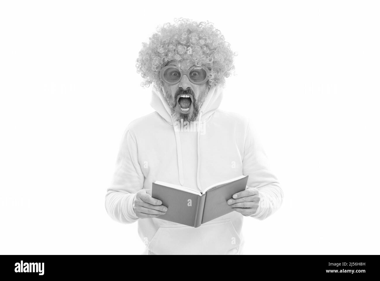 Geeky bibliophile dans la perruque funky garder la bouche ouverte lecture livre d'école, bibliothèque Banque D'Images