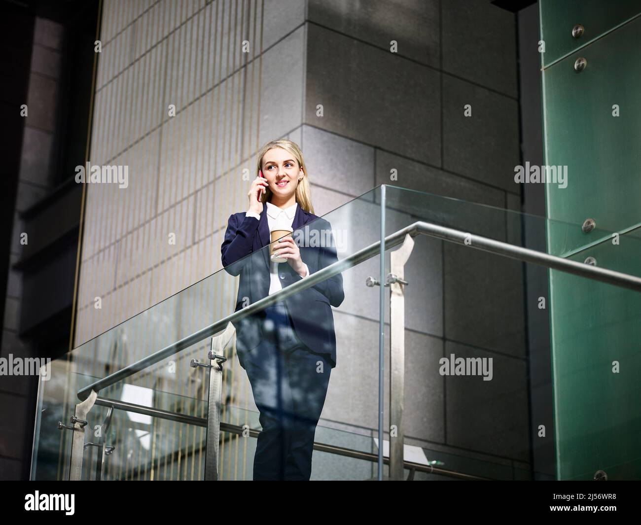 jeune femme d'affaires caucasienne se tenant au-dessus des escaliers faisant un appel en utilisant le téléphone cellulaire dans un immeuble de bureau moderne Banque D'Images