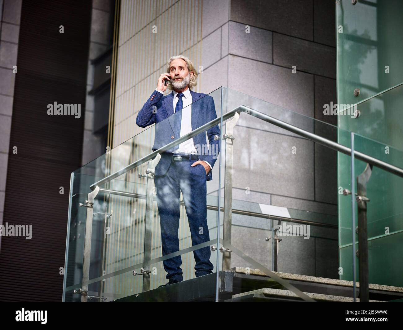 homme d'affaires caucasien mature se tenant au-dessus des escaliers faisant un appel à l'aide d'un téléphone cellulaire dans un bâtiment de bureau moderne Banque D'Images