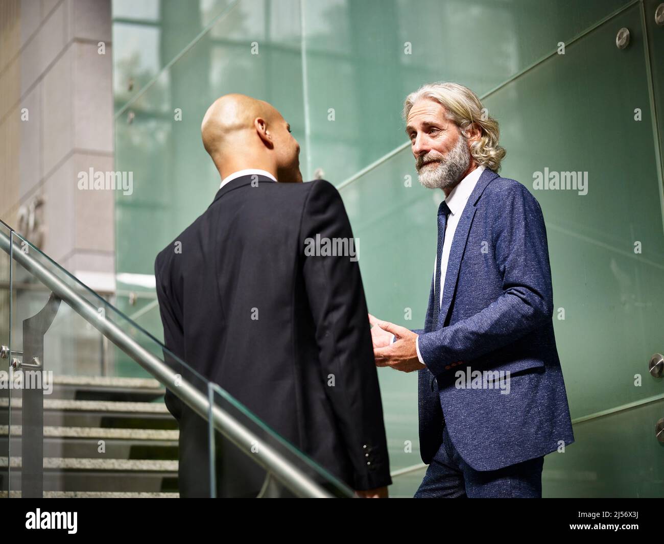 les hommes d'affaires caucasiens et latinos parlent en discutant en marchant dans les escaliers dans un immeuble de bureaux moderne Banque D'Images