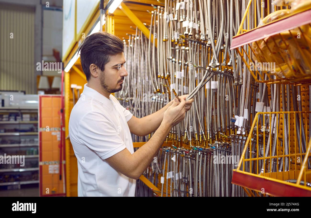 L'homme en atelier choisit des tuyaux d'eau flexibles avec bec en métal pour raccorder l'équipement de plomberie. Banque D'Images